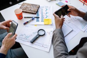 Two professionals analyzing data and graphs with smartphones on a white table.